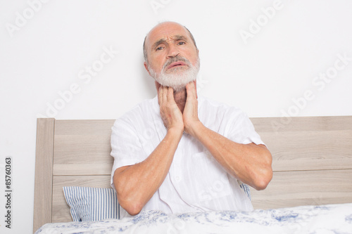 Elderly man sitting on bed suffering from throat problems photo