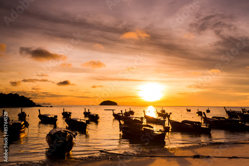 Silhouette fisherman boat with sunrise in tropical beach of Thailand.