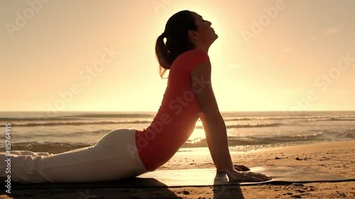 Woman doing yoga on beach in sunset.