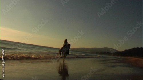 Woman on horse at seashore, riding through surf