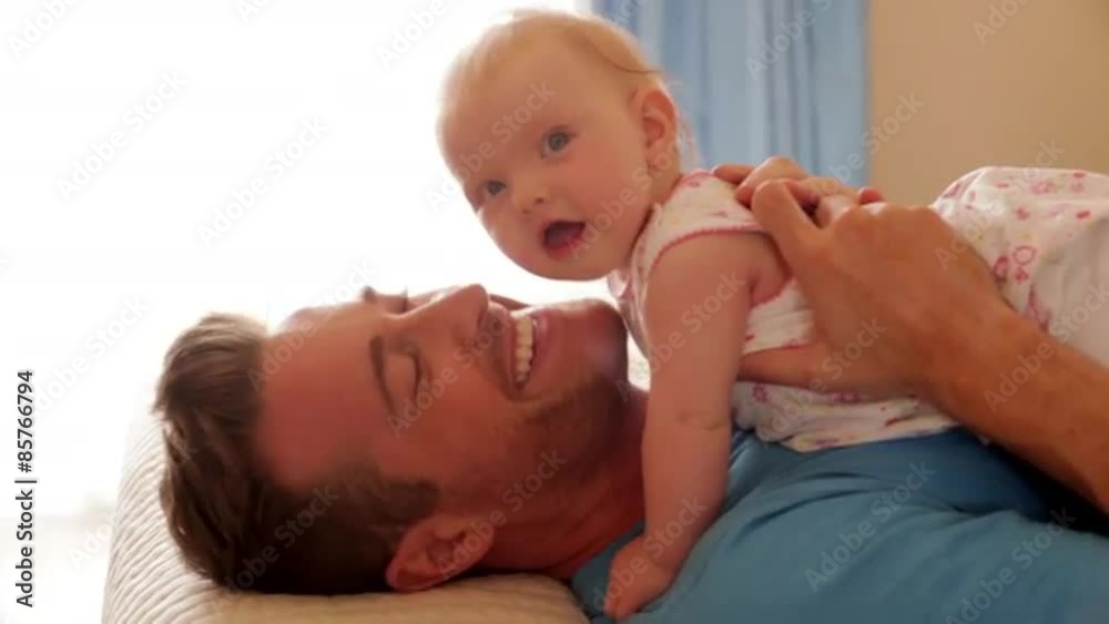 Side view of father on bed with baby daughter. Side view of father on bed with baby daughter.