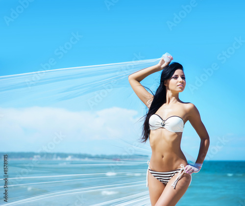 Young, sporty and happy woman posing with a blowing silk on a summer beach