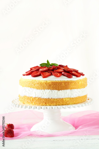 Sweet cake with strawberries on cake stand on white wooden backg