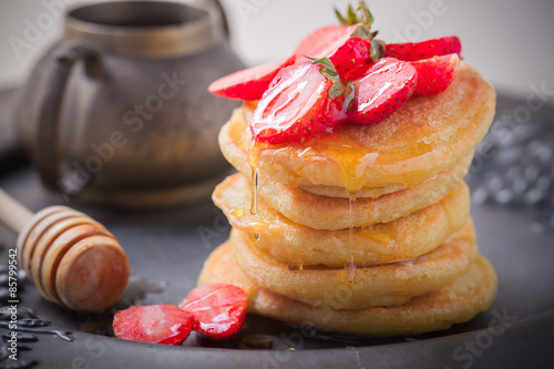 Stack of sweet pancakes with strawberry and honey.