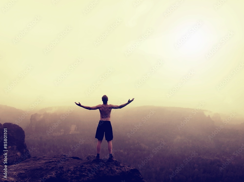 Climber in black pants. Gesture of triumph. Naked tourist on the peak of sandstone rock in national park Saxony Switzerland watching into misty landscape.