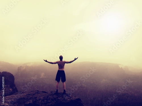 Climber in black pants. Gesture of triumph. Naked tourist on the peak of sandstone rock in national park Saxony Switzerland watching into misty landscape.