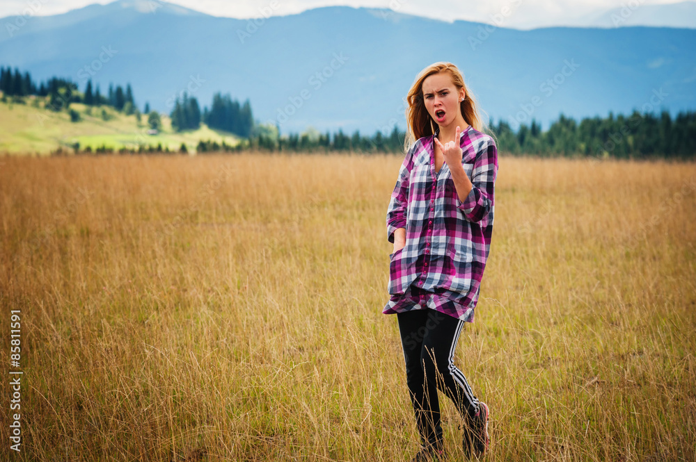 Young woman stand on yellow field and shows rocker gesture