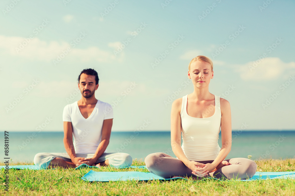 smiling couple making yoga exercises outdoors