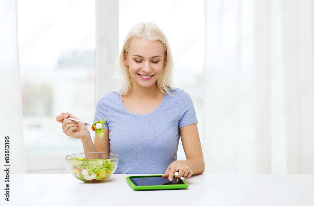 smiling woman eating salad with tablet pc at home