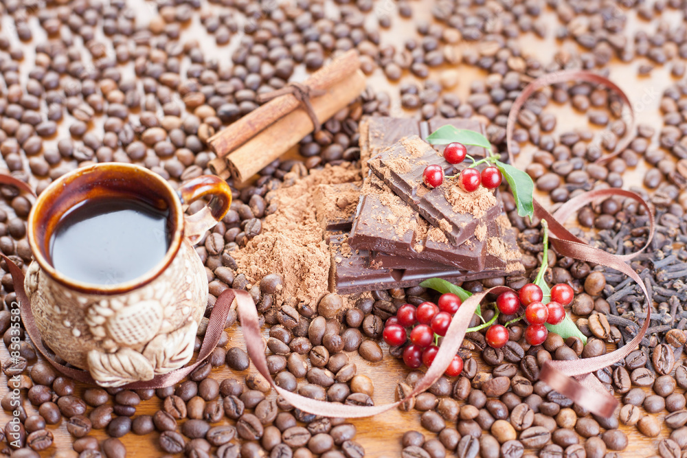 Fototapeta premium Background of chocolate bar, a cup of coffee, cinnamon sticks, hazelnuts, cranberries and coffee beans scattered on the wooden table. Day chocolate and coffee daily. Brugge - Belgian chocolate capital