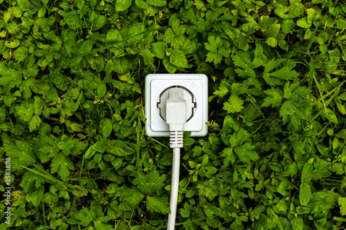 Weiße Steckdose mit Kabel auf grüner Wiese