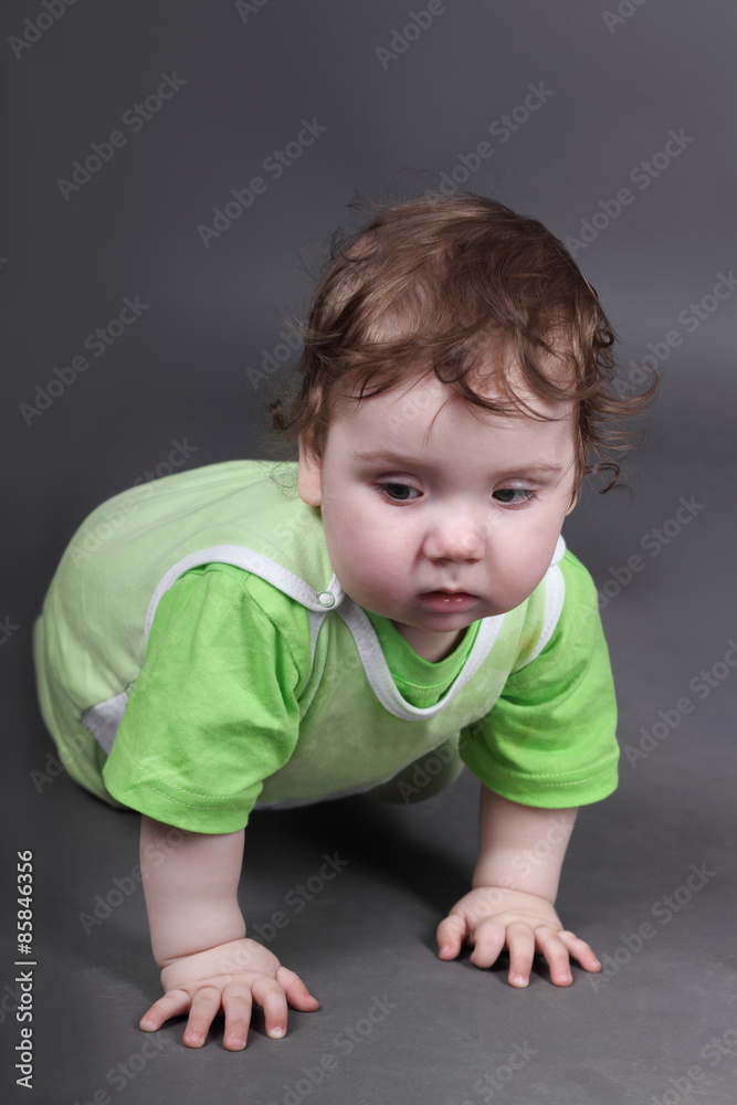 Handsome little baby boy in green crawls on floor in grey studio Handsome little baby boy in green crawls on floor in grey studio