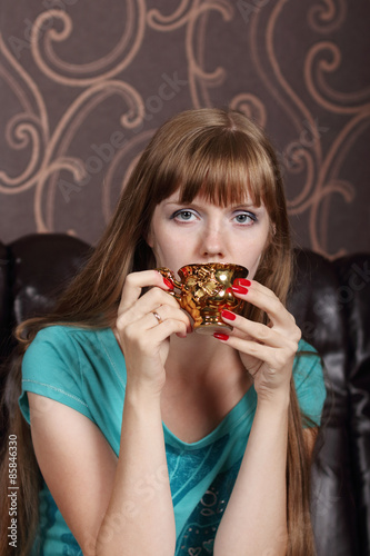 Young beautiful woman drinks coffee from gilt cup on couch 