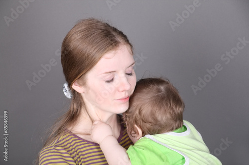 Pretty young mother holds her little baby son in green