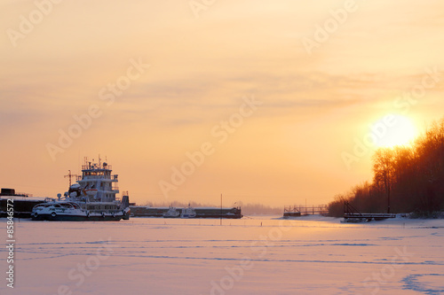 Beautiful sunset with yellow horizon over ship in frozen river © singulyarra