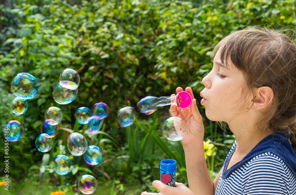 Little girl inflates soap bubbles in the garden