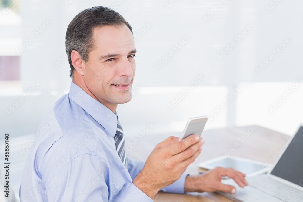 Smiling businessman sending a text at his desk Smiling businessman sending a text at his desk