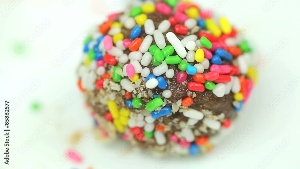 Tasty chocolate cookie ball covered in colorful sugar sprinkles, shot closeup rotating in a seamless loop
