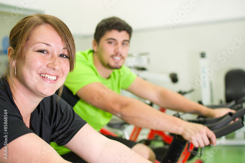 man and woman with stationary bicycle in gym
