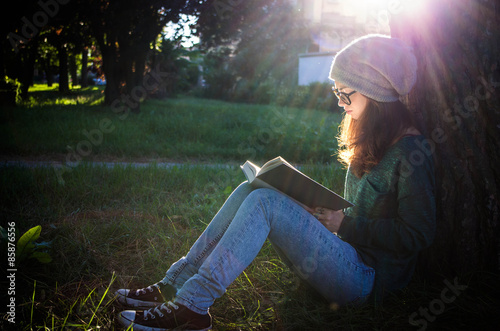 girl reading a book leaning against a tree photo