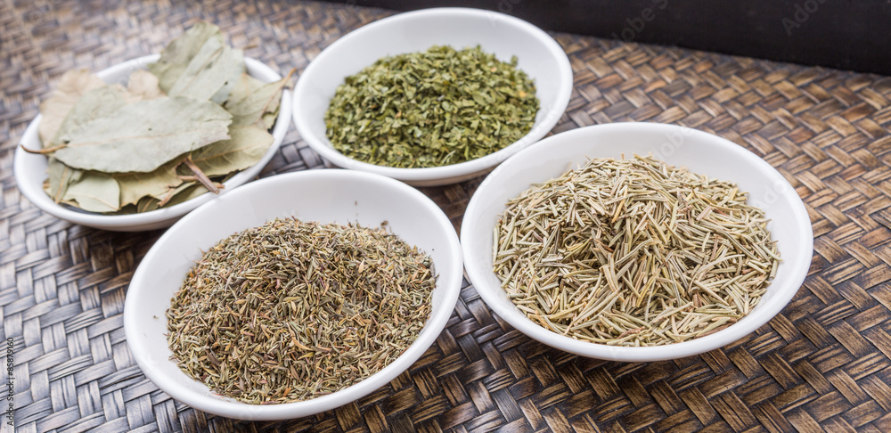 Rosemary, parsley, bay leaves and thyme in white bowl over wicker background Rosemary, parsley, bay leaves and thyme in white bowl over wicker background