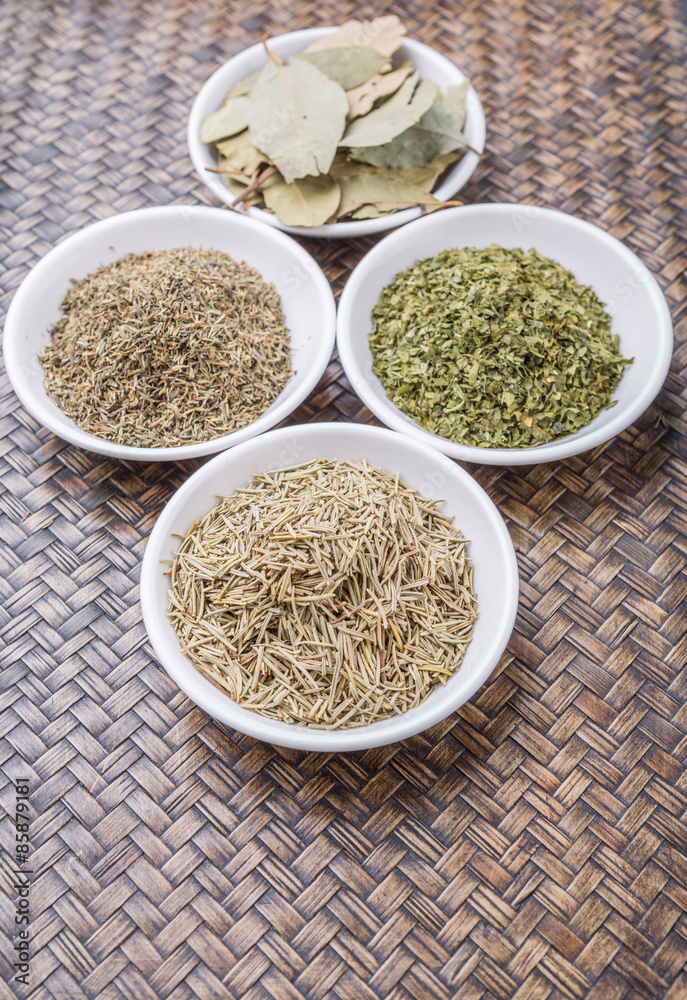 Rosemary, parsley, bay leaves and thyme in white bowl over wicker background Rosemary, parsley, bay leaves and thyme in white bowl over wicker background