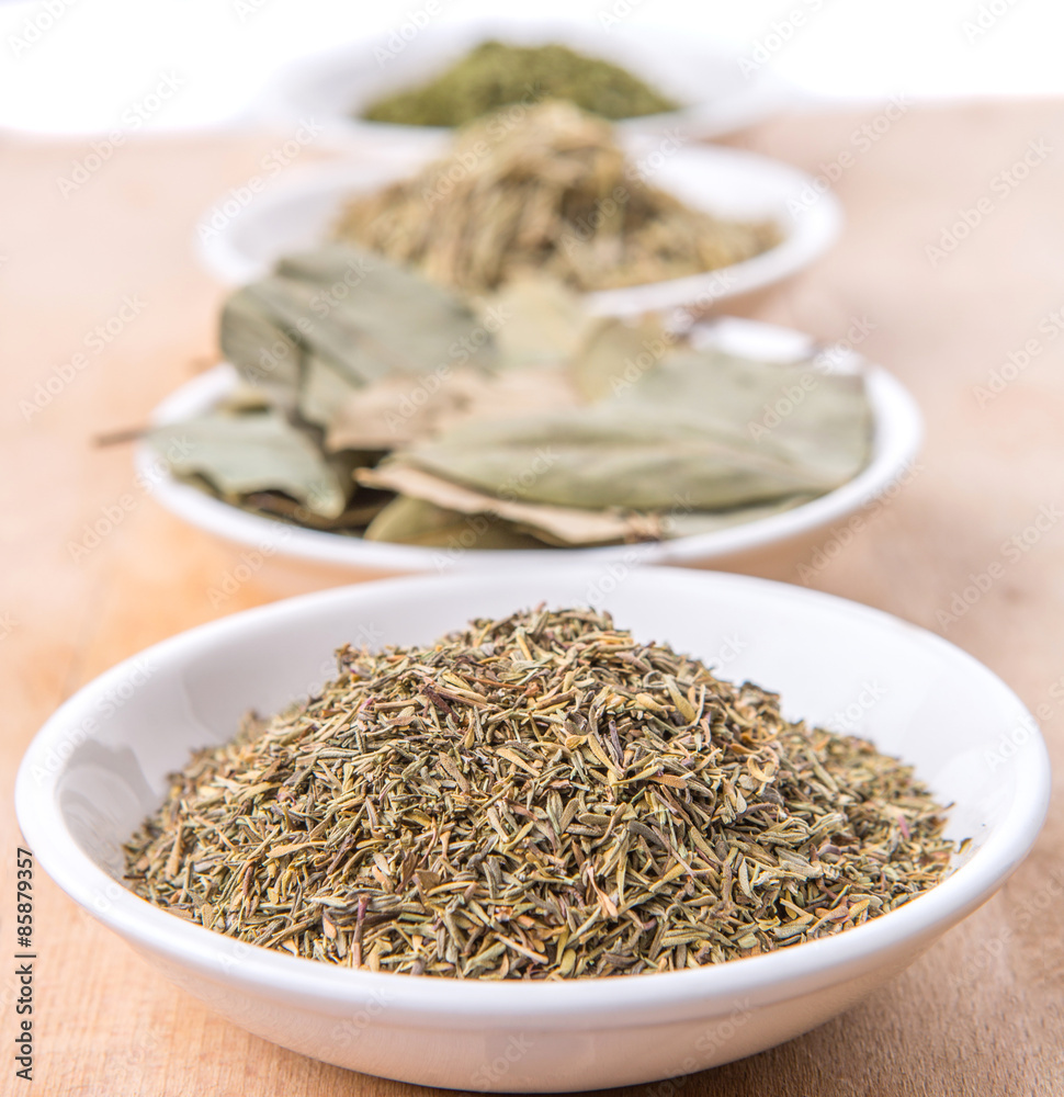 Rosemary, parsley, bay leaves and thyme in white bowl over wooden background Rosemary, parsley, bay leaves and thyme in white bowl over wooden background