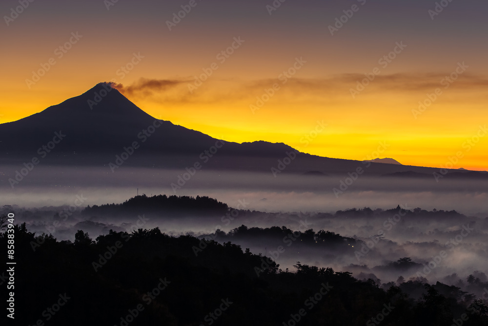 Colorful sunrise over Merapi volcano and Borobudur temple in mis