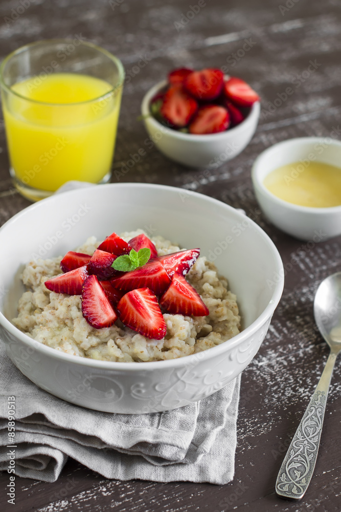 oatmeal with strawberries in a white bowl and orange juice on a dark wooden background oatmeal with strawberries in a white bowl and orange juice on a dark wooden background