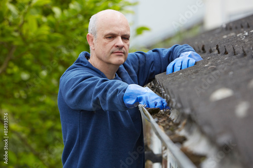 Man Clearing Leaves From Guttering Of House