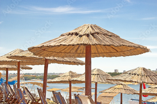 Fototapeta Naklejka Na Ścianę i Meble -  Rows of reed umbrellas and deck chair on beach