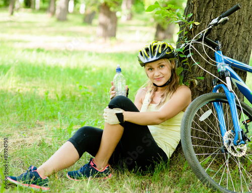 young girl with a bottle water in his hand is resting after cycl photo