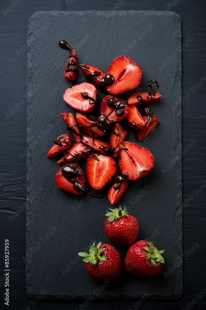 Ripe strawberries with chocolate on a stone slate dish, top view