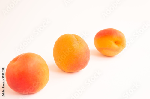 Close up of Three Soft Fresh Apricots Arranged Diagonally on a White Background