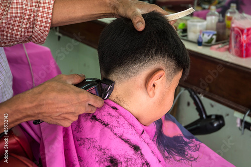 Barber cutting boy hair with electric razor at a barber shop