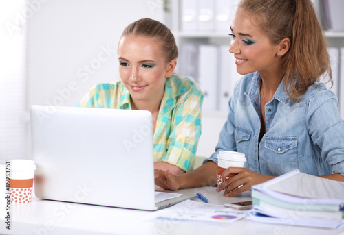 Two women working together at office, sitting on the desk