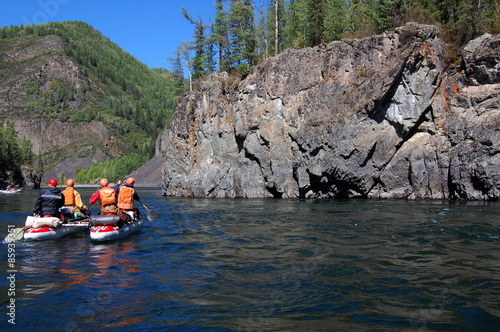 Team of people on an inflatable catamaran raft on a river canyon.
