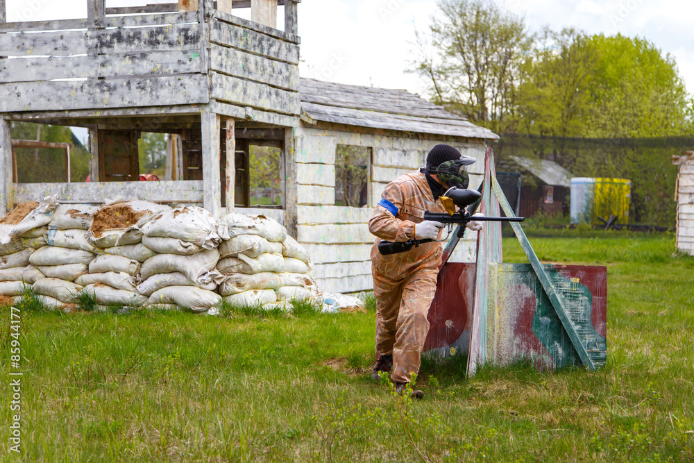 Fototapeta premium Paintball warrior with paint gun and fortress behind