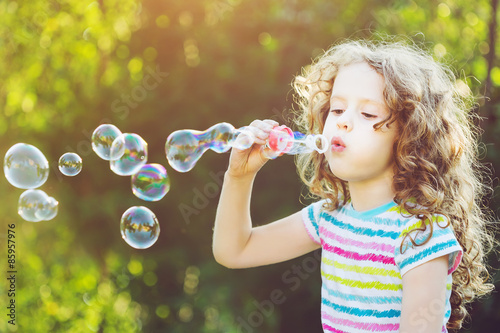 Valokuvatapetti Cute girl blowing soap bubbles, closeup portrait.