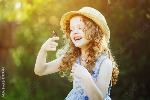 Canvas Print Laughing curly girl with a butterfly on his hand. Happy childhoo