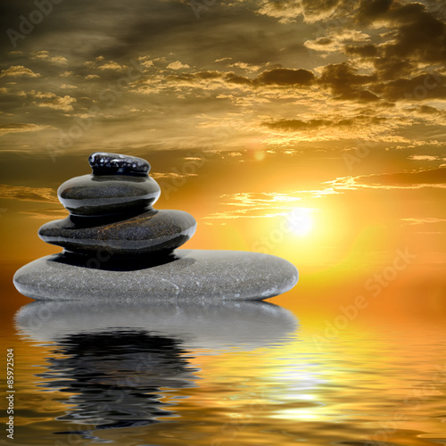 Zen spa concept background - Zen massage stones at sunset reflected in water