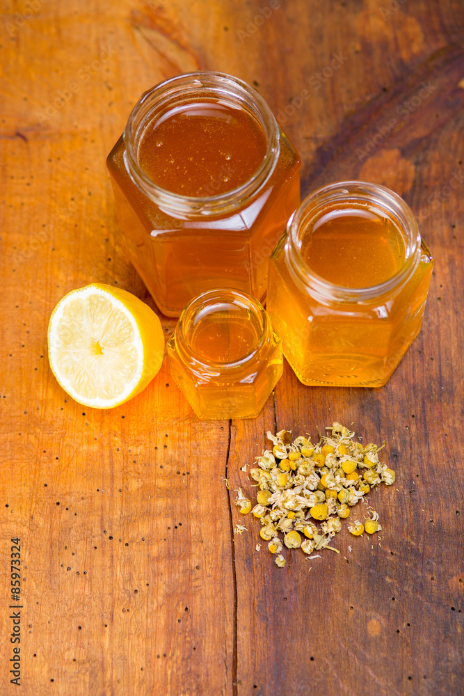 honey in a glass with label on a wooden table with chamomile tea and lemon
honey in a glass with label on a wooden table with chamomile tea and lemon