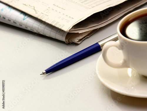 Cup of coffee, pen and newspapers on the desk