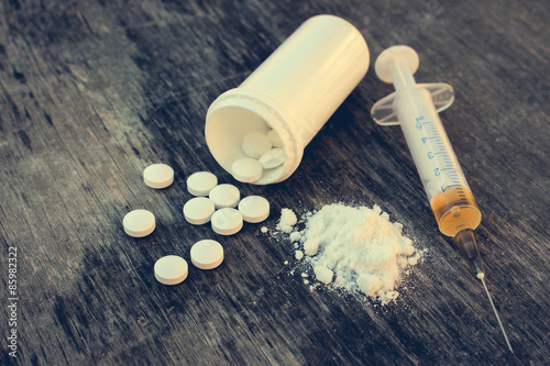 drug addiction on the old wooden background. White pill, syringe and heroin. Toned image. 