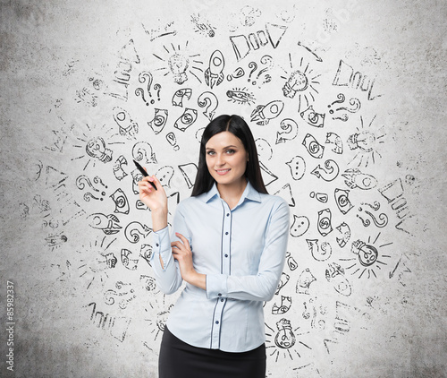 Portrait of smiling woman who points out business icons which are drawn on the concrete wall. photo