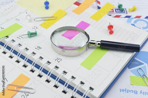 Magnifying glass with colorful post It notes and pin on diary pa