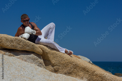 Молодой спортивный брутальный мужчина в боксерских перчатках на море. Мужчина в белых брюках. 