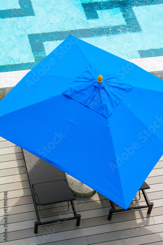 beach chair and blue umbrella by the pool