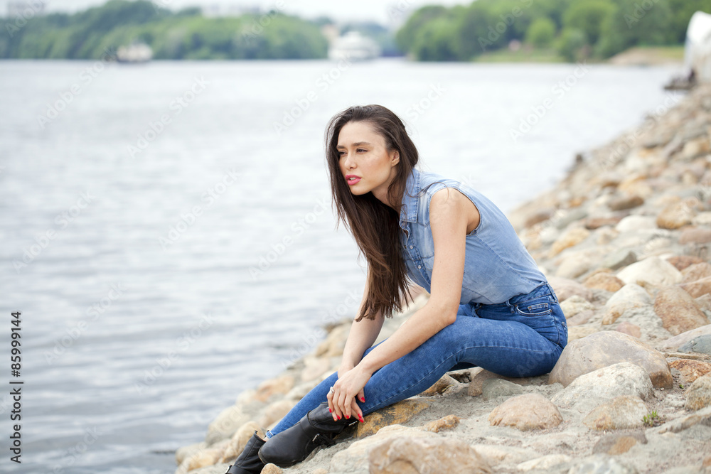 Young beautiful brunette girl sitting on the rocks on the river