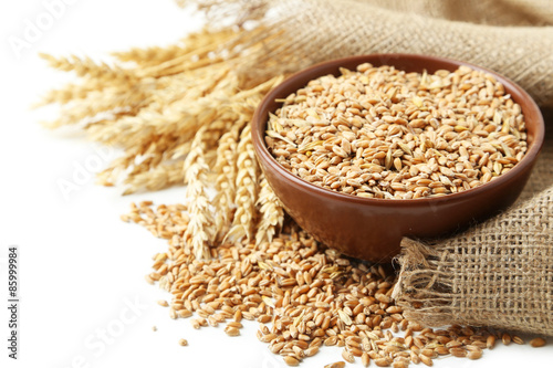 Ears of wheat and bowl of wheat grains on white background